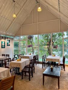 a dining room with tables and chairs and windows at Ban Mali Cafe & Riverside Stay in Ban Chang