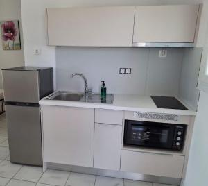 a white kitchen with a sink and a microwave at Gorgona apartments & studios in Ipsos
