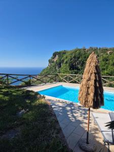 a pool with a straw umbrella and a table and chairs at La Cicogna in Agerola