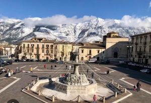 a city with a fountain and mountains in the background at Holidays House Il Vicoletto in Sulmona