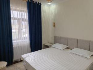 a bedroom with a large bed with blue curtains and a window at Ibrohim Xoja Hotel in Khiva