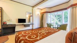 a bedroom with a bed and a desk and a television at Lillium Hotel & Spa in Kalimpong