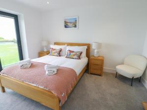 a bedroom with a bed with a chair and a window at Glynllifon 5 in Llanallgo