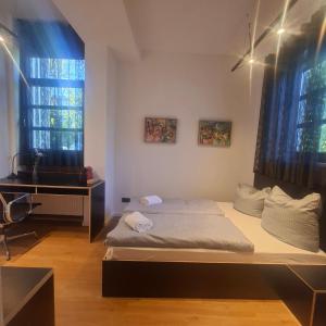 a bedroom with a bed and a desk and two windows at Estelada Studios Unterhaching in Unterhaching