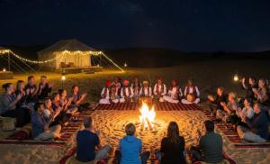 a group of people sitting around a fire in the sand at Golden Celestial haveli jaisalmer in Jaisalmer