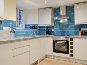 a kitchen with white cabinets and blue tiles at Tarn Rigg Cottage - Uk1368 in Keswick
