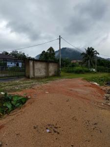 a dirt road with a fence and mountains in the background at IBY II Homestay in Ketereh