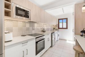 a kitchen with white cabinets and a tv on the wall at Villa FLEUR in Cala en Porter