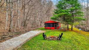 a red cabin in the woods with two chairs and a fire at Creekside Hideaway in Laurelville +32 photos