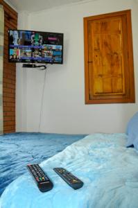 dos controles remotos en una cama con TV en la pared en Estalagem Terramauá, en Visconde De Maua