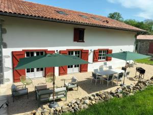 a patio with tables and chairs and green umbrellas at Maison basque de charme avec piscine in Souraïde
