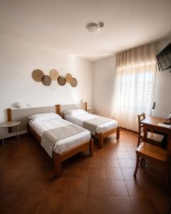 una camera da letto con due letti, un tavolo e una finestra di Hotel Mistral ad Alghero Altre 14 foto