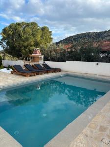 a swimming pool with lounge chairs next to a wall at Villa Pano Salamina in Ambelákia
