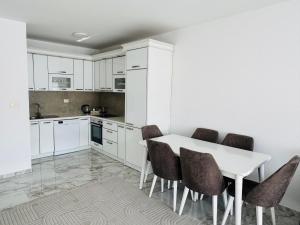 a kitchen with white cabinets and a white table and chairs at Rubinas Apartment in Prizren