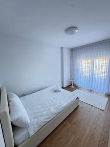a white bedroom with a bed and a window at Rubinas Apartment in Prizren
