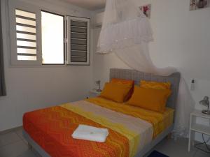 a bedroom with a bed with orange pillows and a window at LAPALOMADESANSEs in Les Anses-dʼArlets