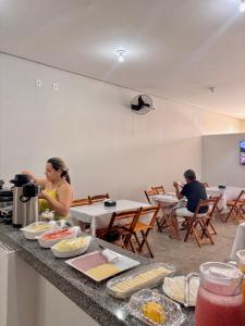 a woman sitting at a table with food on a counter at Pousada Lua Bela in Piranhas