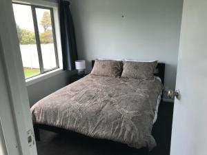a bed with a gray comforter and a window at Cosy Beach House in Riverton