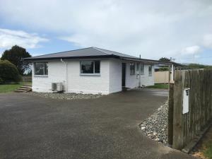 a white house with a fence in front of it at Cosy Beach House in Riverton