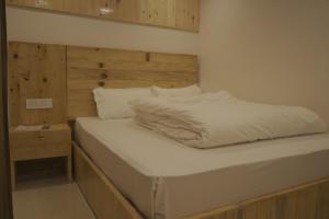 a bed with a wooden headboard and white sheets at Bhagirathi Homestay in Joshīmath