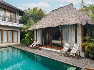 a villa with a pool and chairs next to a house at ZIN Berawa Villas & Bungalows in Canggu
