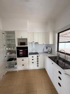 a kitchen with white cabinets and a sink and a window at Ferguson House in Cessnock