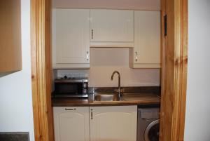 a kitchen with white cabinets and a sink and a microwave at Swallows Barn Cottage in North Rode