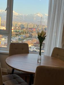 a table with a vase of flowers on it in front of a window at Designer Apartment with Mountain View in Almaty +11 photos