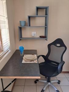 ein Schreibtisch mit einem Stuhl und einem Tisch mit Tellern darauf in der Unterkunft Coco 's Hamlet Flatlet in Prince Alfreds Hamlet