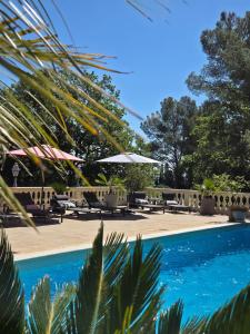 a swimming pool with chairs and umbrellas and trees at Villa Manoe in Draguignan