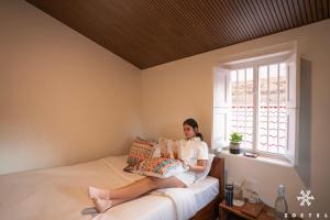 a woman sitting on a bed reading a book at Zostel Ooty, Pudumund in Ooty