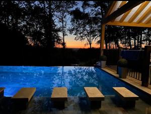 a pool with benches and a sunset in the background at Villa de Standing, Climatisation, Piscine chauffée & Nature in La Chapelle-Saint-Aubin