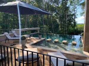 a deck with a pool with chairs and an umbrella at Villa de Standing, Climatisation, Piscine chauffée & Nature in La Chapelle-Saint-Aubin