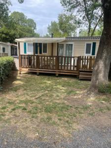 a house with a wooden porch with a tree at Mobilhome Ligaropa climatisé 3 ch 6 pers camping des 7 fonts in Agde