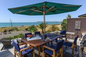 uma mesa e cadeiras de madeira com um guarda-sol na praia em Absolute Beachfront B&B em Napier