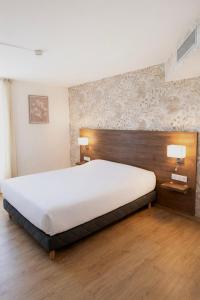 a bedroom with a large white bed with a wooden headboard at Hôtel Restaurant Le Relais - Pau Nord in Lons