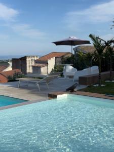a swimming pool with chairs and an umbrella at Viscalori Homes in Viagrande