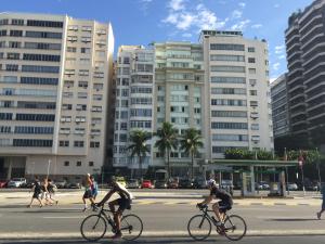 dos personas montando bicicletas por una calle con edificios altos en Atlantica Lofts, en Río de Janeiro