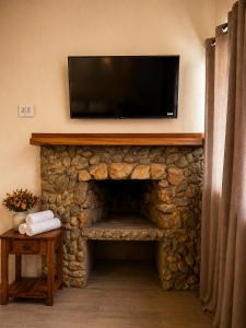 a living room with a stone fireplace with a flat screen tv at Refúgios de Mauá - Chalé Jardins de Maria in Visconde De Maua