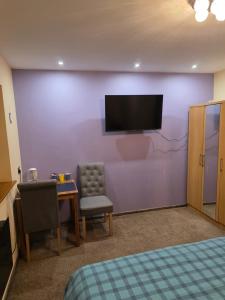 a bedroom with a purple wall with a tv and a chair at Lux House in Peterborough