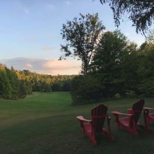 three red chairs sitting in a field of grass at The Barn - A Unique Gathering Place in Sainte-Cécile-de-Masham