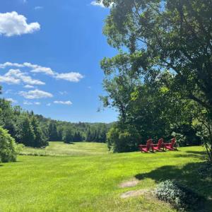 three red park benches in a grassy field at The Barn - A Unique Gathering Place in Sainte-Cécile-de-Masham