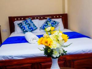 a vase filled with yellow and white flowers on a bed at Dorado Homestay, Chaani in Mombasa