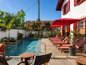 a pool with chairs and tables and a red umbrella at Hôtel Villa Maïtia in Ustaritz