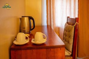 a coffee maker and cups on a wooden table at Equator Lodge & Campsite in Kikorongo