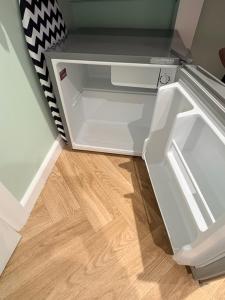 an empty refrigerator with its door open on a wooden floor at Clover Road Guest Suite in Swaffham