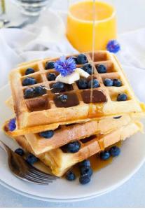 a plate with a stack of waffles with blueberries and syrup at Sun kissed beach haven in Waitarere