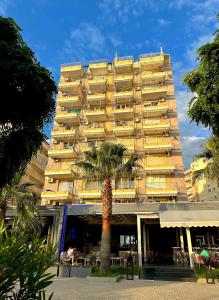 a large yellow building with a palm tree in front of it at Eri Apartments 2 in Shëngjin