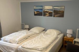 two beds in a room with three paintings on the wall at Moderner Bungalow E25 in Lichtenau