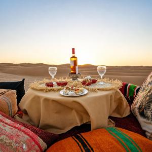 a table with a bottle of wine and wine glasses at Rosara Luxury Camp in Merzouga